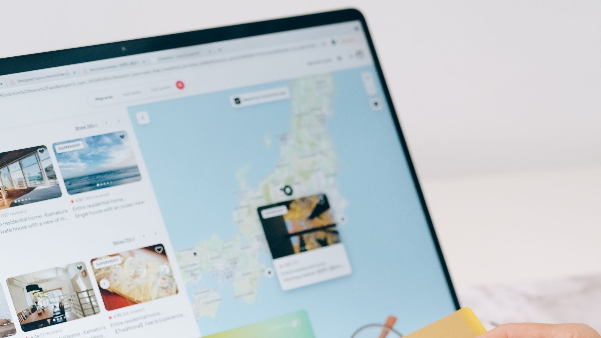 A laptop showing an Airbnb search results page with home listings and an interactive map