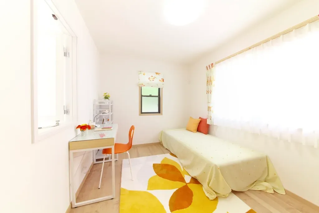 An empty, made-up guest bedroom with a single bed, a small desk and an orange chair.